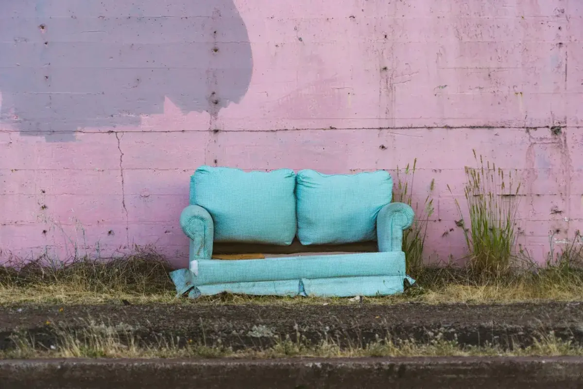 An old two-seater sofa left outdoors against a painted wall.