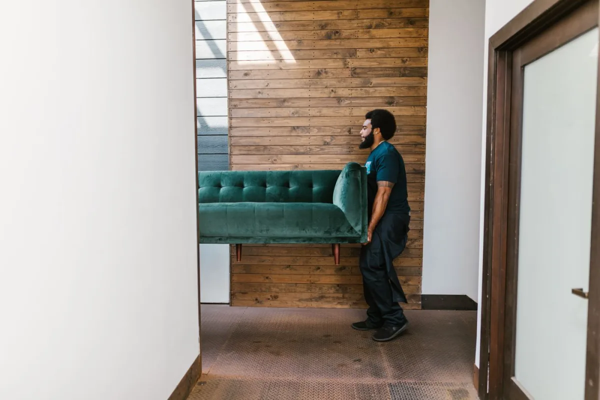 A person carrying a green sofa through a hallway.