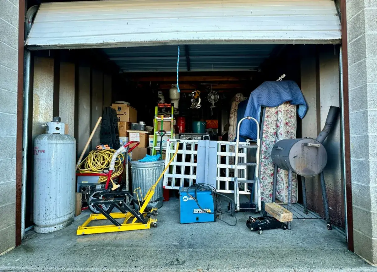 A garage packed to the door with tools, ladders, a mattress and stored household items.
